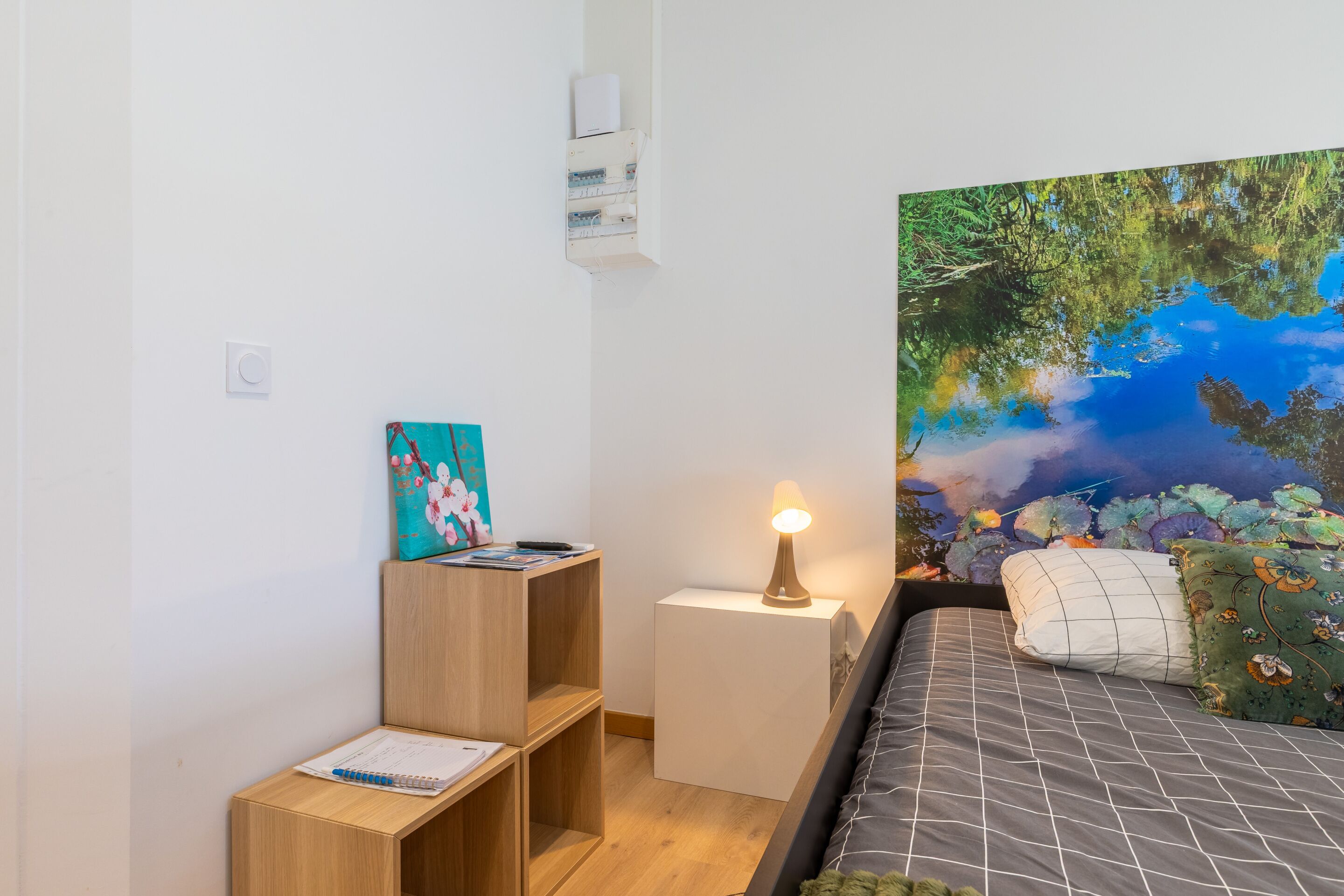 A bedroom with a bed, a nightstand, a wooden shelf, and a wall-mounted air conditioner.