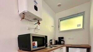 Une cuisine compacte avec des meubles blancs, un four à micro-ondes, une machine à café et un petit réfrigérateur.