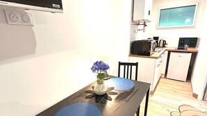 Une cuisine compacte équipée d’un four à micro-ondes, d’une cuisinière et d’un réfrigérateur. Une table à manger, entourée de chaises, et un vase de fleurs se trouvent au centre de la pièce.