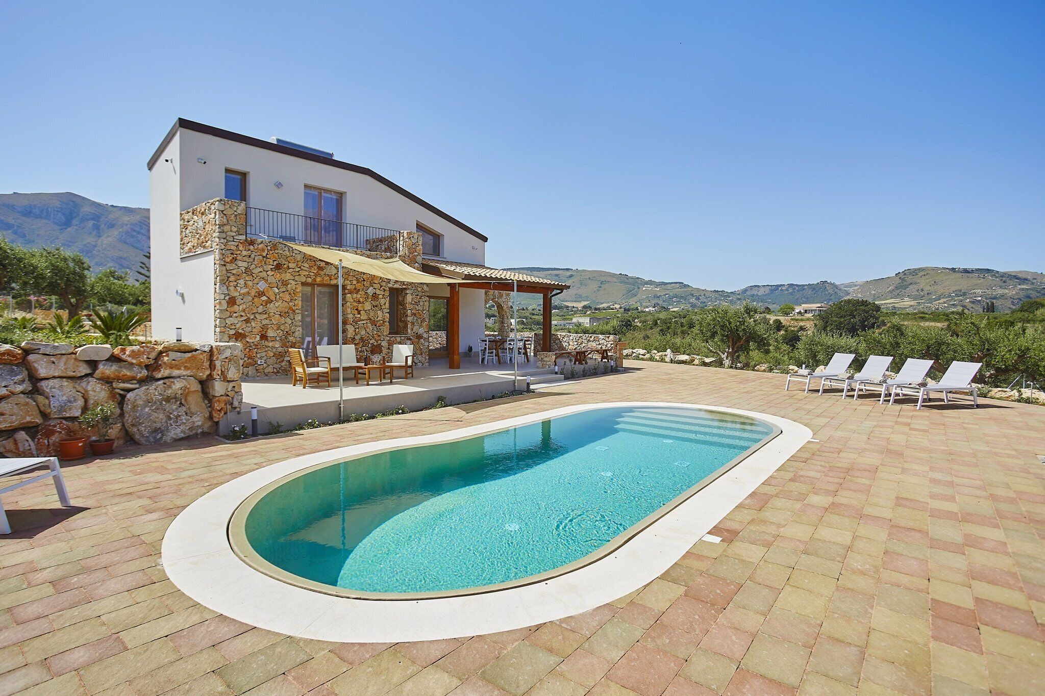 A modern house with a swimming pool, stone facade, and a patio with lounge chairs.