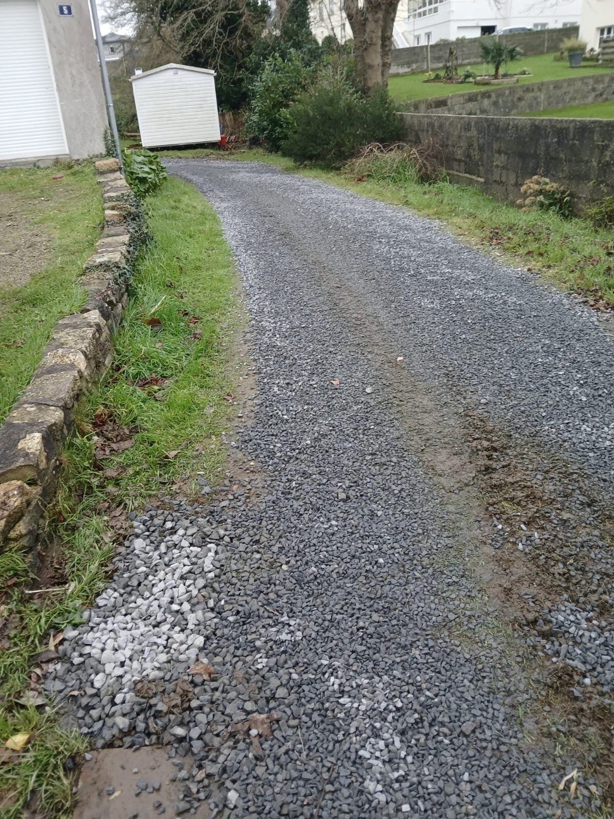 Een grindpad dat leidt naar een wit gebouw met een garage.
