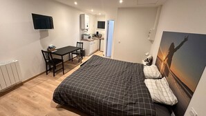 A bedroom with a bed, a desk, a chair, a TV, and a kitchenette. - Ancrage New Studio Garden Floor (Plouedern)