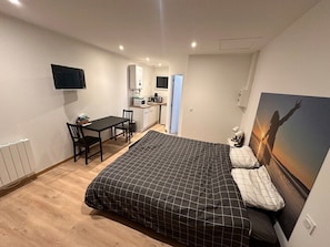 Ein Schlafzimmer mit Bett, Schreibtisch, Stuhl, Fernseher und einer Küchenzeile.