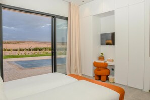 A modern hotel room with a large bed, a TV mounted on the wall, and a sliding glass door leading to a garden with a pool. - Aggafay experience in Palais Maya (Marrakesh)