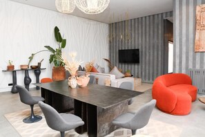 A modern living room with a dark wooden dining table, grey upholstered chairs, a red sofa, and a flat-screen TV mounted on the wall. - Aggafay experience in Palais Maya (Marrakesh)