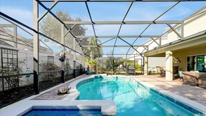 Une piscine dotée d’une enceinte en verre, entourée d’un patio aménagé avec des meubles d’extérieur et des plantes.