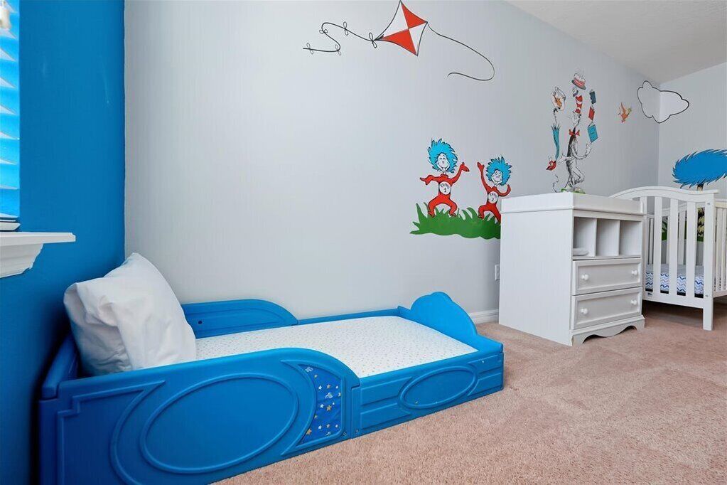 Ein Kinderzimmer mit Etagenbett, Babybett und Wanddekorationen, darunter ein Drachen und Zeichentrickfiguren.