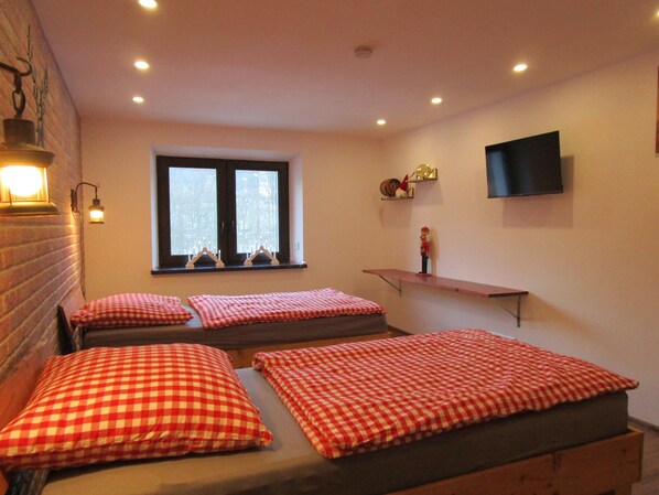 Una habitación con dos camas, una ventana, un televisor y una estantería con objetos.