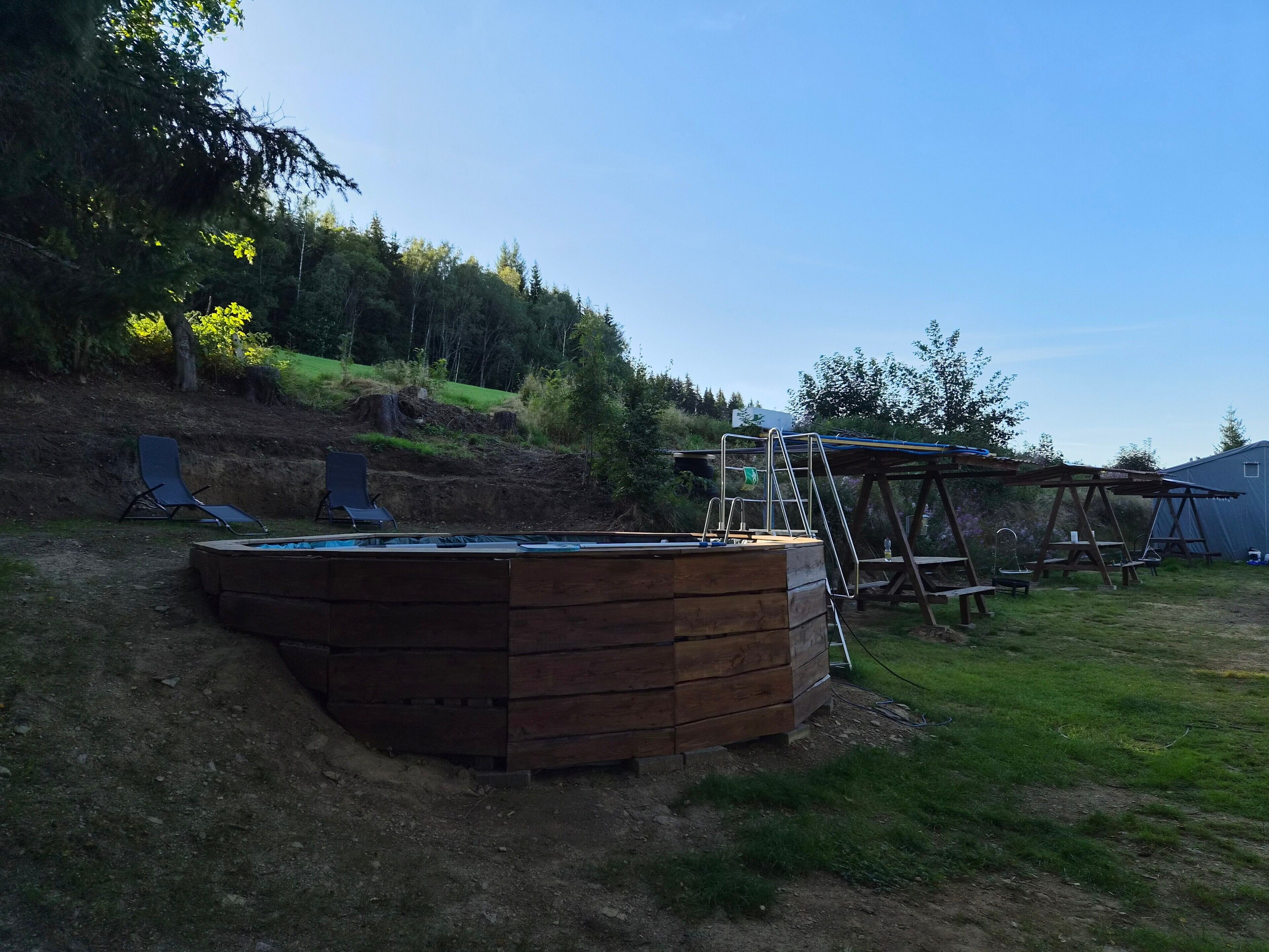 En træterrasse med pool, gyngestativ og et overdækket picnicområde.