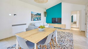 Un soggiorno moderno con un tavolo da pranzo in legno, sedie grigie, un quadro di grandi dimensioni, una TV e una parete di colore verde acqua.