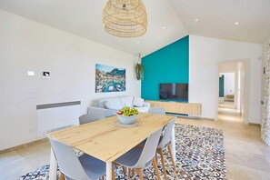 A modern living room with a wooden dining table, grey chairs, a large painting, a TV, and a teal accent wall. - Villa Azzurra Scopello | Infinity Pool Retreat | Steps from Village and Tonnara (Castellammare del Golfo)
