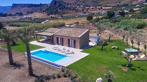 Una casa con piscina, immersa in un prato curato e circondata da palme.