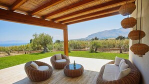 Zona salotto esterna coperta con mobili in vimini e vista su vigneti e montagne.