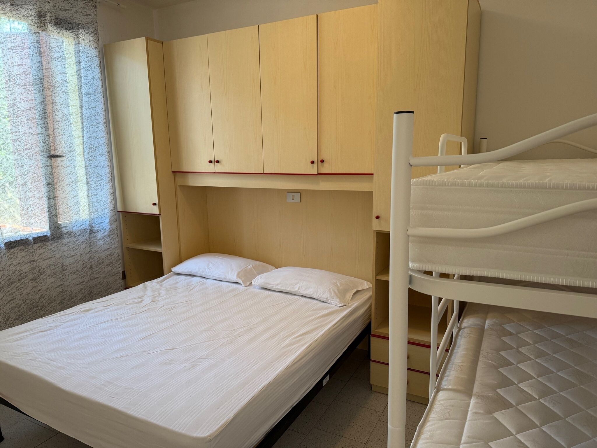 Een slaapkamer met een stapelbed, een enkel bed en een houten garderobe.
