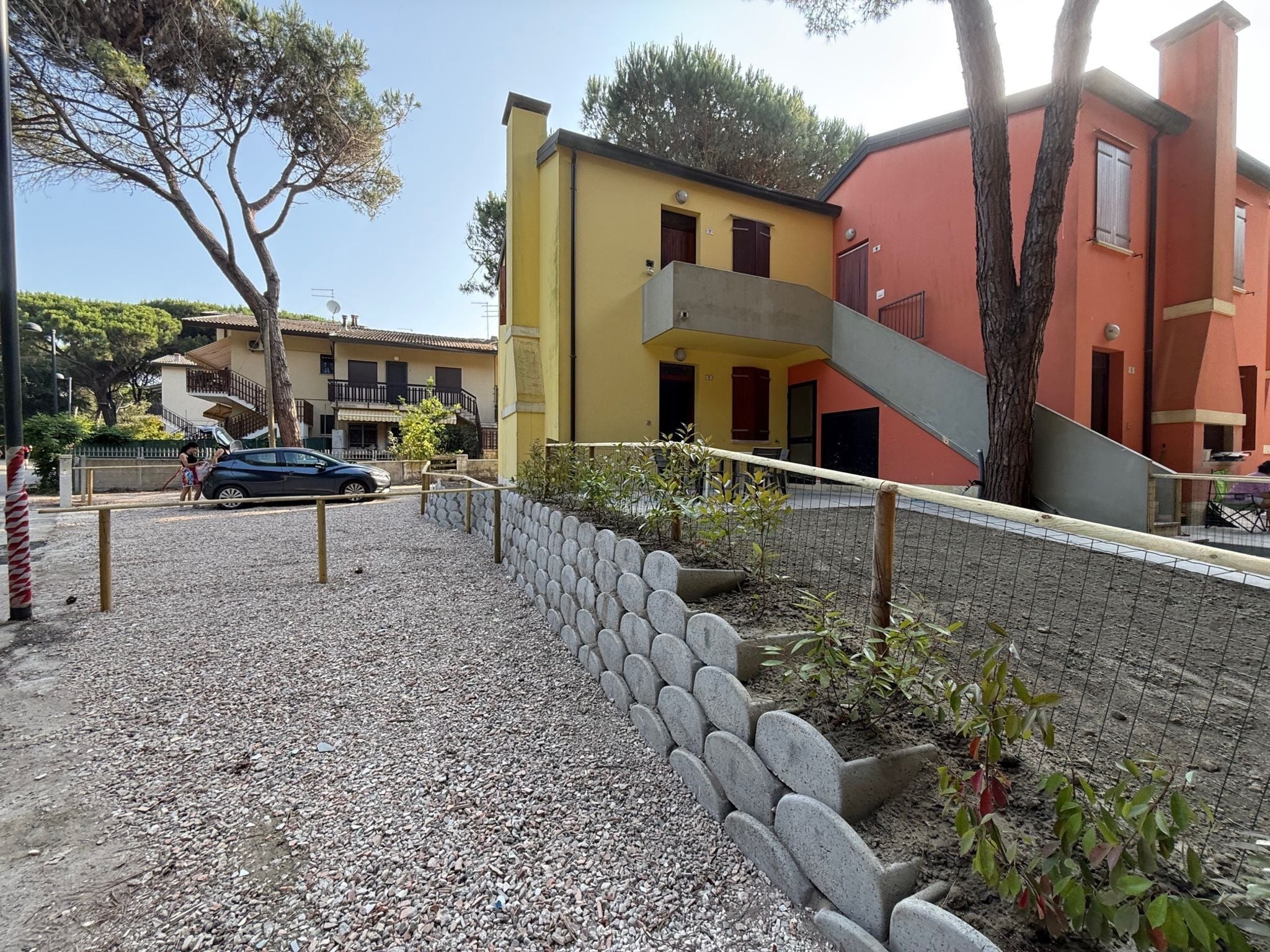A residential area with a yellow building, a red building, and a blue car parked in front.