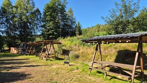 Un espace extérieur rustique agrémenté de structures en bois, notamment une balançoire et un coin salon abrité.