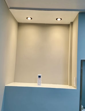 A small, enclosed room with a beige wall and a blue accent wall. There is a white object on a shelf in the corner.