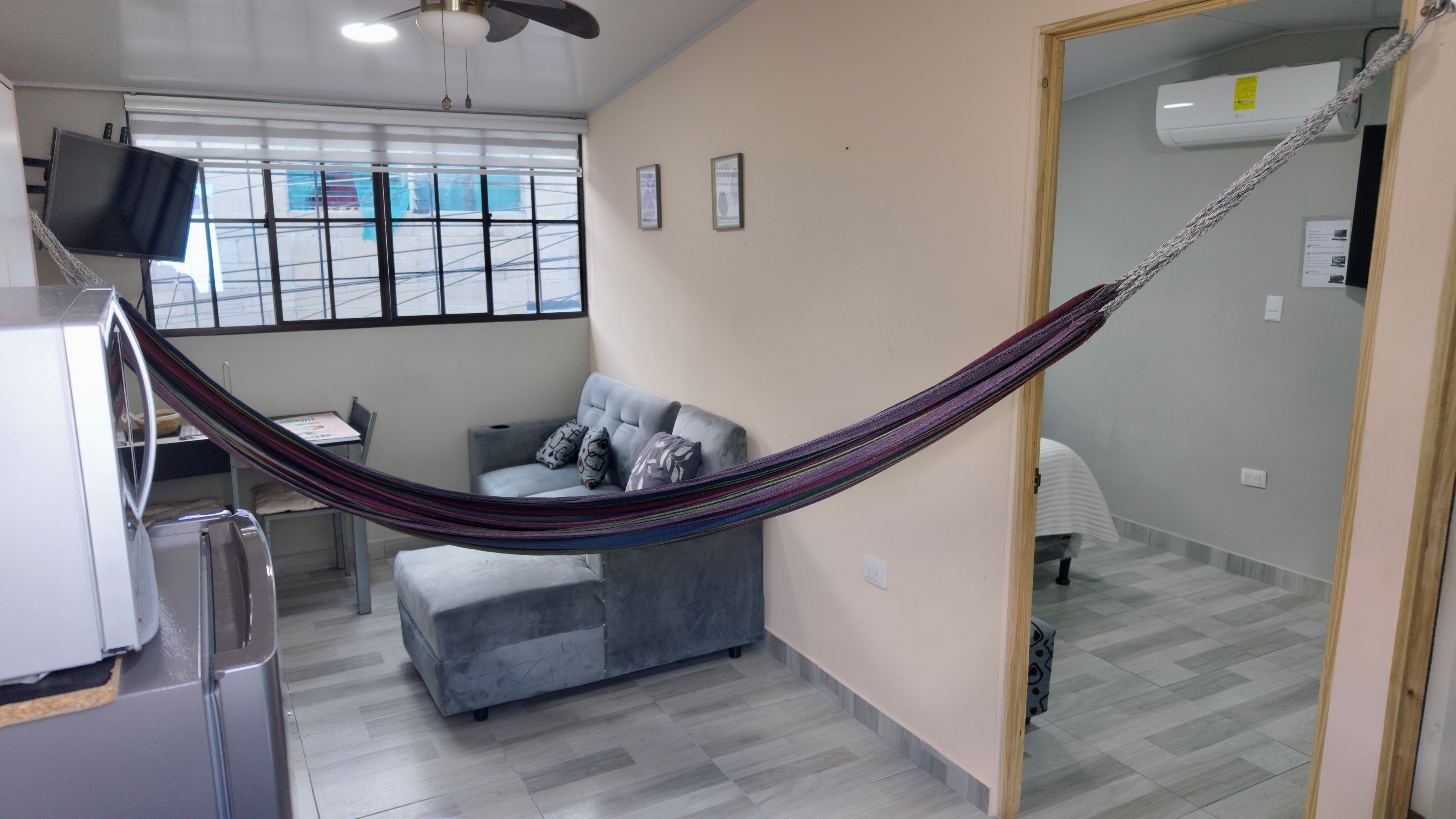 A modern living room with a grey sofa, a hammock, a flat-screen TV, and a refrigerator.