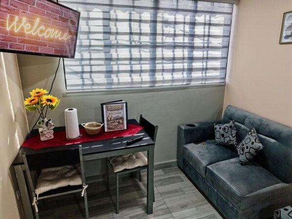 A room with a red table, a book, a vase with sunflowers, a grey couch, and a 'Welcome' sign.
