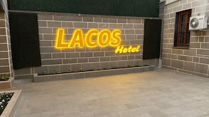 Señal de A LACOS Hotel sobre un muro de ladrillo con un patio empedrado.