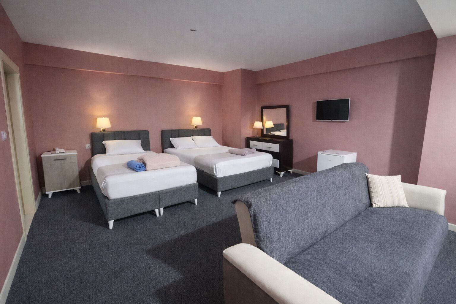 Et hotelværelse med to senge, en sofa, et fjernsyn og et natbord med lampe.