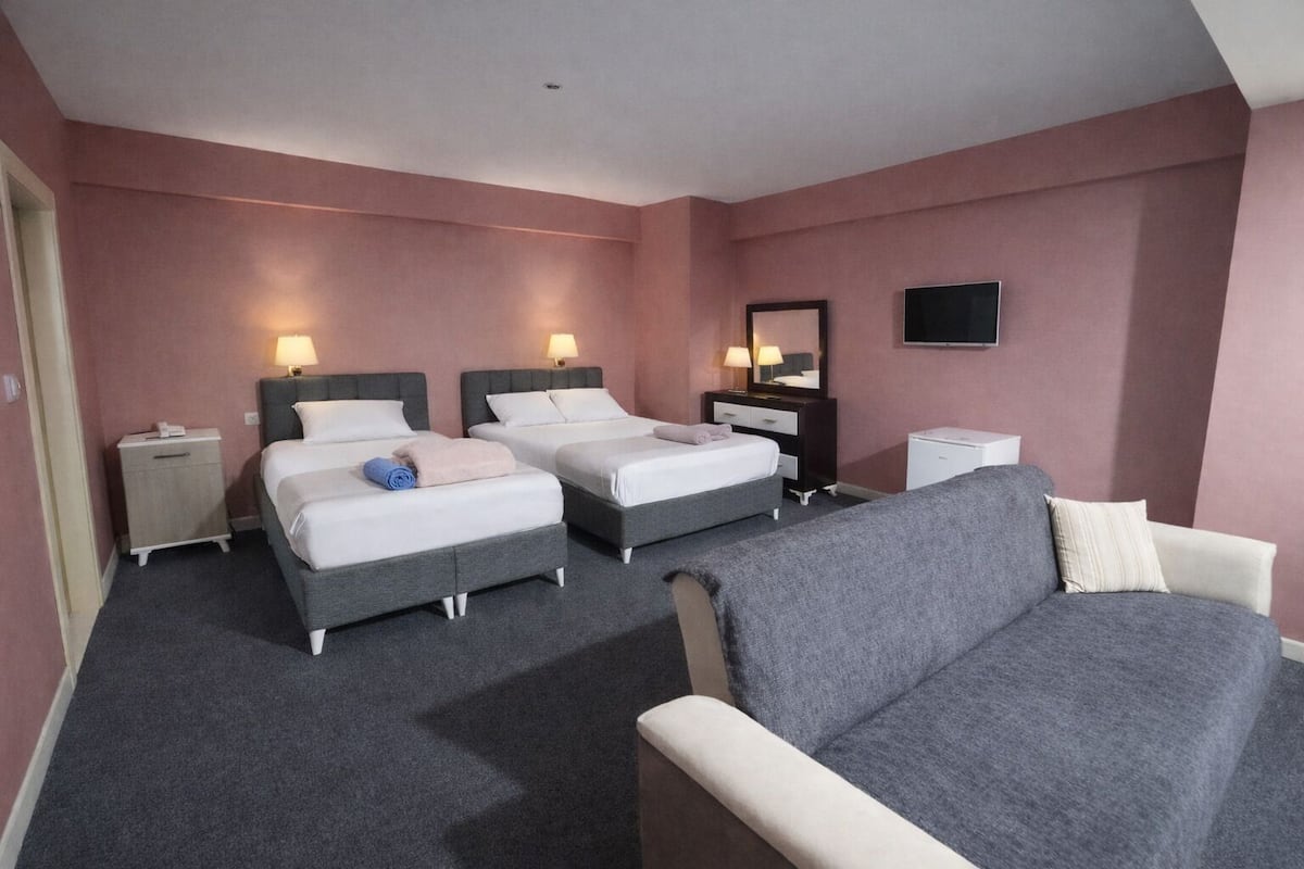 A hotel room with two beds, a sofa, a TV, and a bedside table with a lamp.