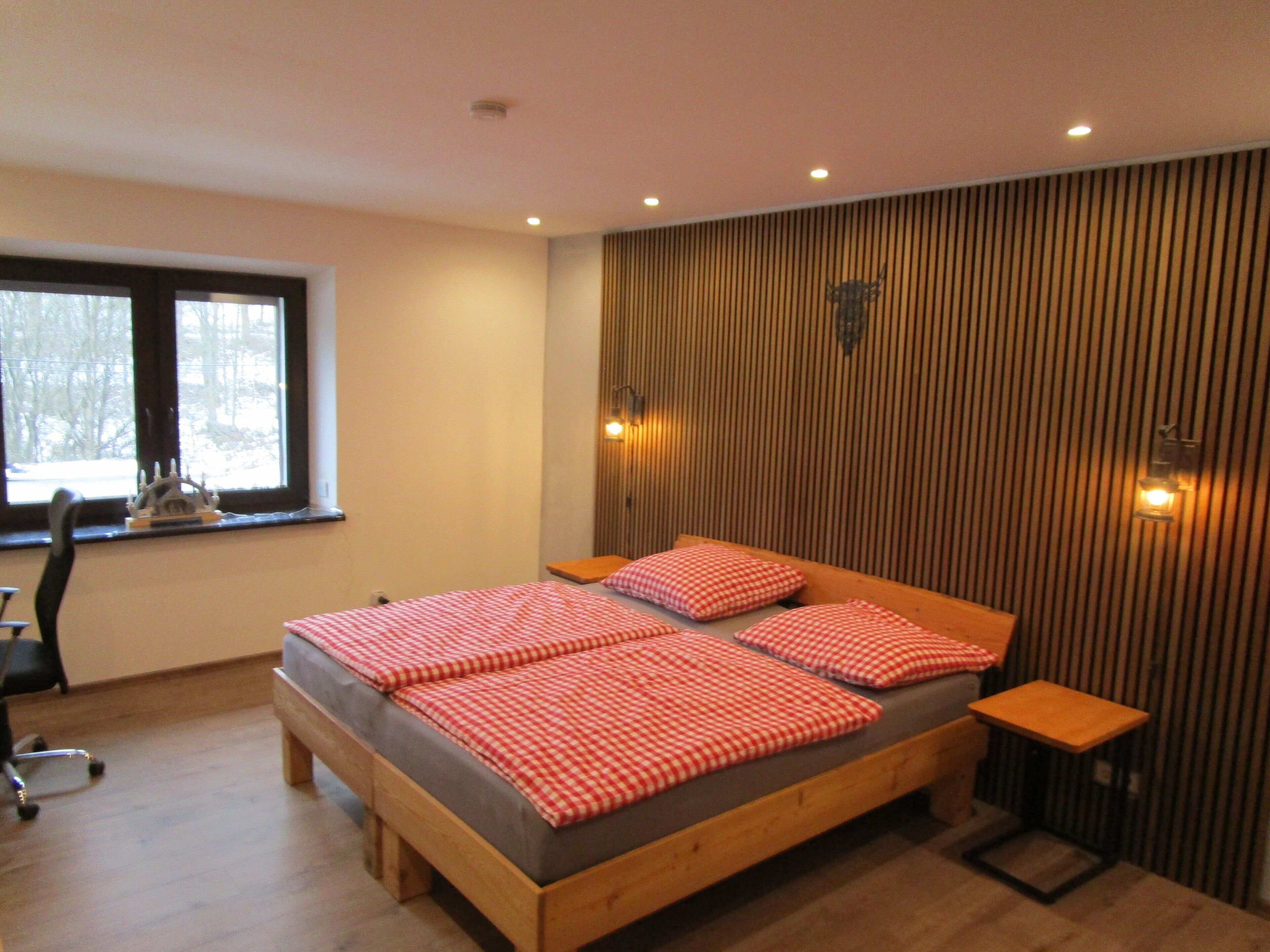 Une chambre à coucher avec un lit en bois, une literie à carreaux, une fenêtre, un bureau et une chaise.