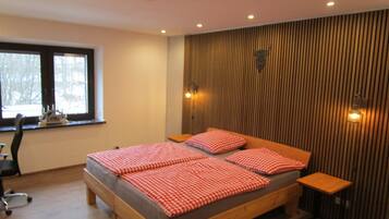 Une chambre à coucher avec un lit en bois, une literie à carreaux, une fenêtre, un bureau et une chaise.
