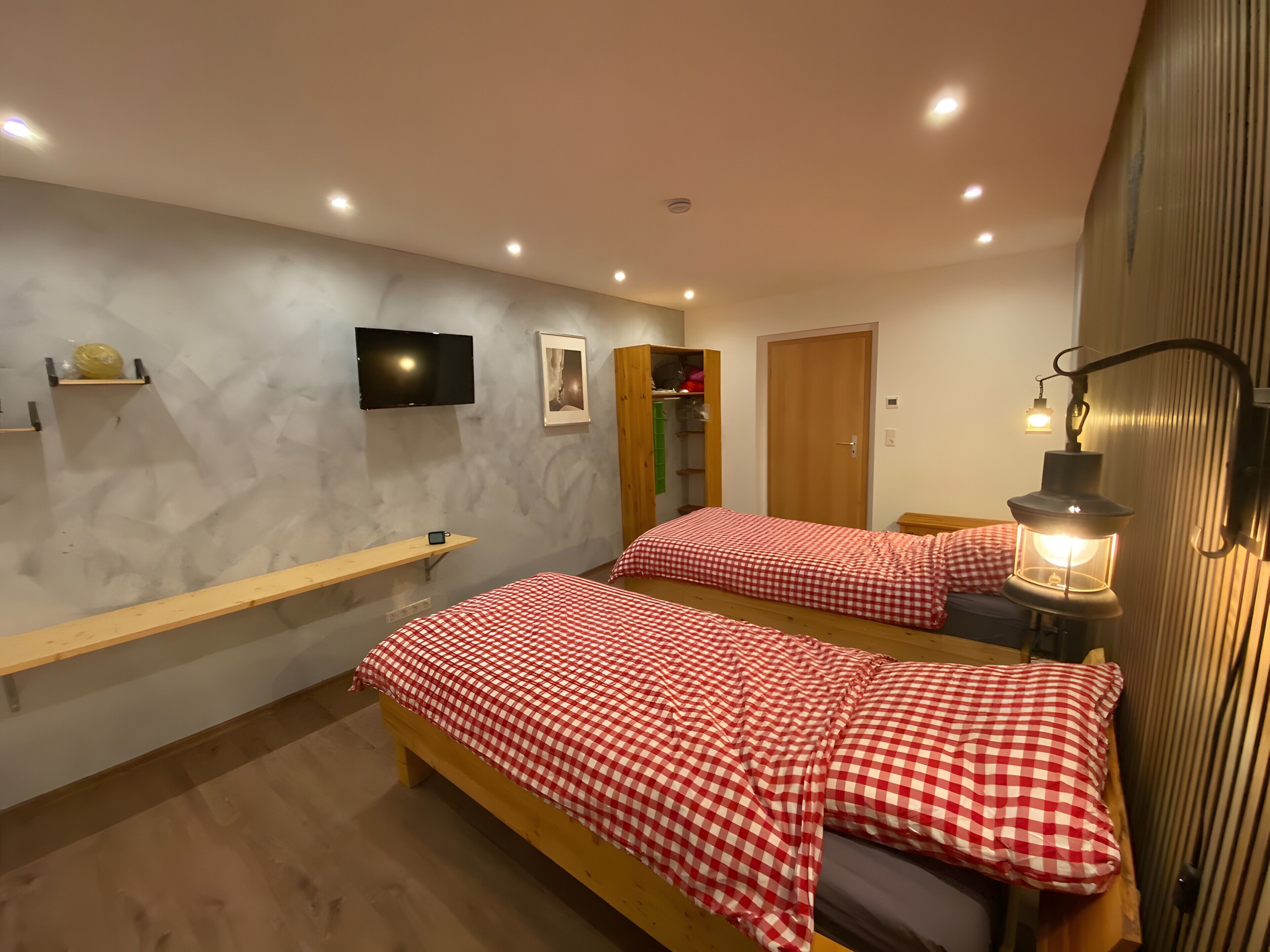 Une chambre avec deux lits, une télévision, une étagère, une armoire et une lampe de chevet.