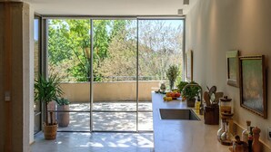 Eine moderne Küche mit einem großen Schiebeglasfenster, das auf einen Balkon führt, einer Marmorarbeitsplatte sowie verschiedenen Küchengeräten und Pflanzen.