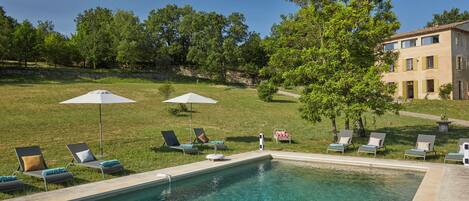 A swimming pool with lounge chairs and umbrellas, surrounded by a grassy area and trees.