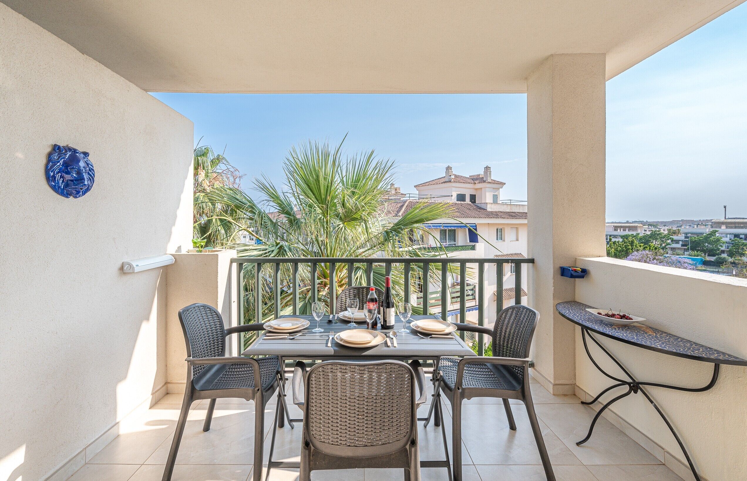 A balcony with a table set for two, chairs, a small table, and a decorative item on the wall.