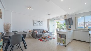 En moderne stue med spiseplads, sofa, sofabord og et køkken med et fjernsyn.