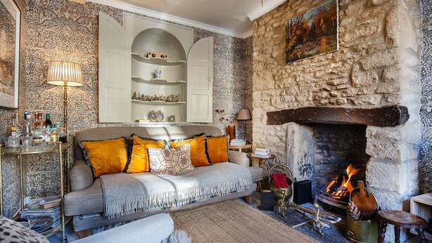 Uma sala de estar acolhedora com lareira de pedra, sofá com almofadas estampadas e uma estante decorativa.