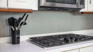 Una cocina con gabinetes blancos, un microondas de acero inoxidable y una estufa a gas.