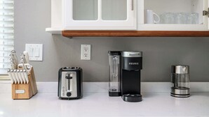 Una encimera de cocina con un tostador, una cafetera Keurig, una jarra de vidrio y un bloque de cuchillos.