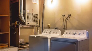 Zona de lavandería con lavadora y secadora, calentador de agua y contador de servicios.