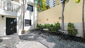 A courtyard with a black door, outdoor seating, palm trees, and a building with a beige wall and windows. - Retro Miami Getaway With Free Parking 1 Minute From Beach (Miami Beach)