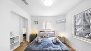 A bedroom with a large bed, a bedside table, a lamp, a window with blinds, and a view of a building outside. - Art Deco Stay 1 Block From Ocean Balcony (Miami Beach)