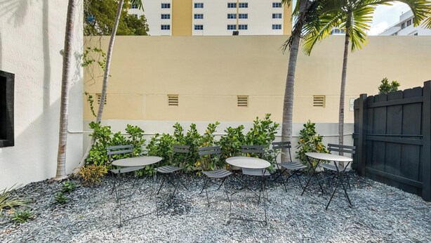 A patio area with tables and benches, surrounded by a low wall and palm trees. - Art Deco Escape Steps to Ocean Free Parking (Miami Beach)
