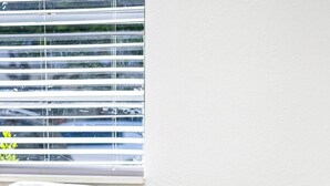 A grey sofa with a cushion, a white metal shelf unit with a plant, and a window with blinds. - Art Deco Escape Steps to Ocean Free Parking (Miami Beach)