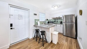 A compact kitchen with a refrigerator, microwave, and a small island with stools. - Casa Mare 1BR Steps From the Ocean (Miami Beach)