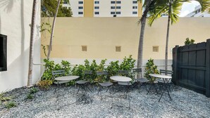 An outdoor patio with tables and chairs, surrounded by plants and a gravel ground. - Casa Mare 1BR Steps From the Ocean (Miami Beach)