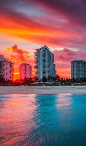 A beachfront hotel with multiple high-rise buildings, a sandy beach, and a sunset sky. - Casa Mare 1BR Steps From the Ocean (Miami Beach)
