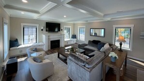 Amplia sala de estar con chimenea, asientos cómodos, televisor de pantalla plana y ventanas grandes.
