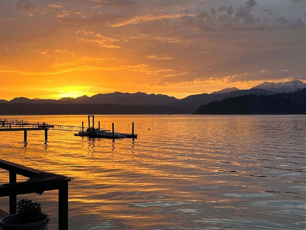 A sunset over a calm lake with a dock and mountains in the background.