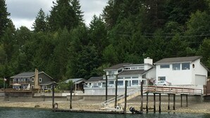 A waterfront property with a dock, a white house with a balcony, and a smaller house in the background. - Hood Canal Waterfront - Dock Hot Tub BBQ Games (Union)