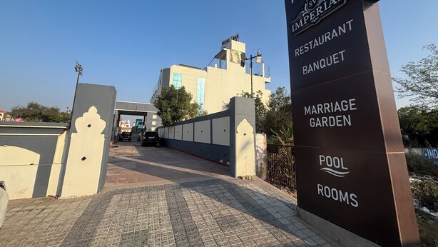 Entrada d'hotel amb un cartell que enumera serveis com ara restaurant, sala de festes, jardí de casaments i habitacions amb piscina.