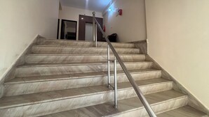 Una escala amb graons de marbre i barana metàl·lica, que condueix a un espai amb una porta i un lluminari al mur.