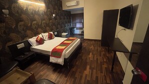 Habitació d'hotel amb llit, taulella de nit, làmpada i televisió penjada a la paret.